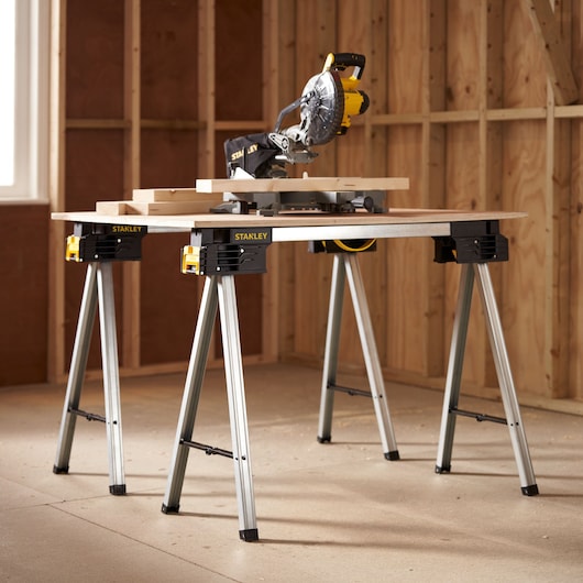 Photo of STANLEY FMST1-75763 work stand with miter saw and wood boards, shown in workshop setting.