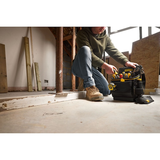 Stanley FMST17624-1 tool bag with yellow tools on construction site, person kneeling beside bag.