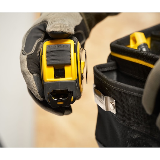 Photo of STANLEY FMST17624-1 tape measure held by a glove with a tool belt in view.
