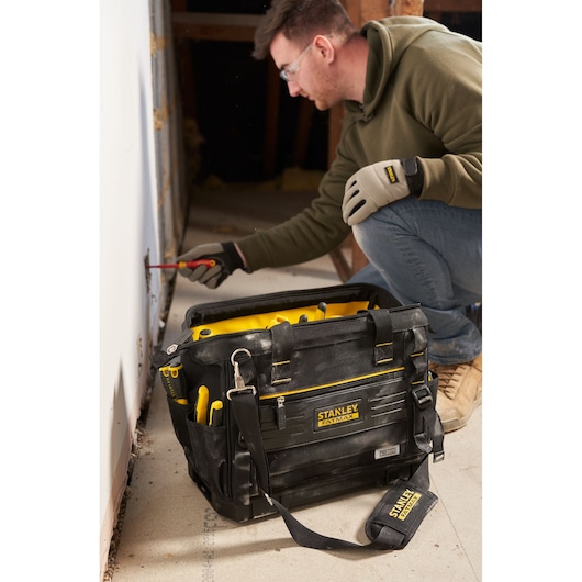 Photo of STANLEY FMST17627-1 tool bag with yellow accents, filled with hand tools, set on a worksite floor.