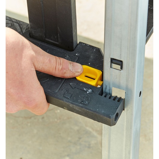 STANLEY FMST81083-1 workbench close-up, hand pressing yellow locking button on black plastic support.
