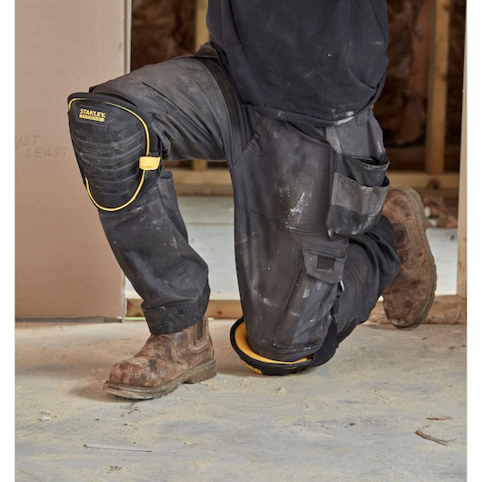 STANLEY FMST82959-1 black and yellow knee pad worn by a person kneeling on a construction site.