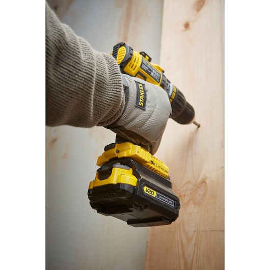 STANLEY SFMCB121D1 cordless drill in use, yellow and black, shown close-up during wood drilling.