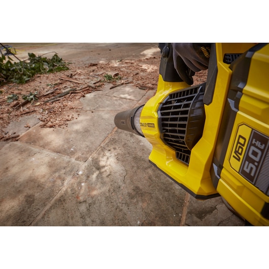 Photo of STANLEY SFMCBLB76B cordless leaf blower clearing debris on a concrete surface, close angle.