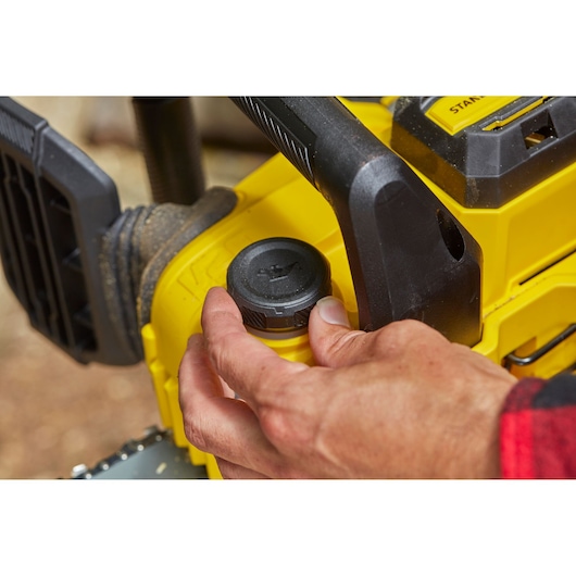 STANLEY SFMCCS630M1 chainsaw close-up, hand adjusting oil cap, yellow and black design, outdoor setting.