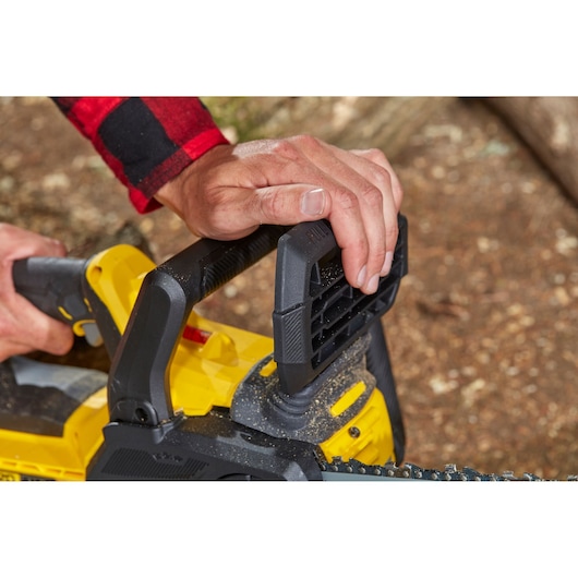Photo of a person using the STANLEY SFMCCS630M1 chainsaw, close-up on hands gripping black and yellow handle.