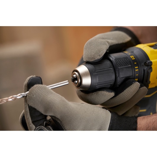 STANLEY SFMCD710C2K cordless drill held in gloved hands, close-up inserting a drill bit.