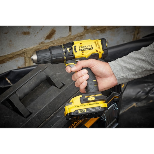 Photo of STANLEY SFMCD711C2S cordless drill, yellow and black, held in hand near tool box.
