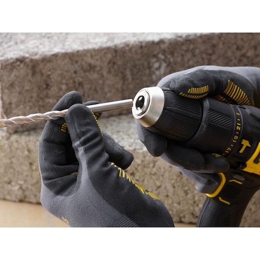 STANLEY SFMCD711C2S cordless drill close-up with gloved hands inserting a drill bit, outdoor setting.