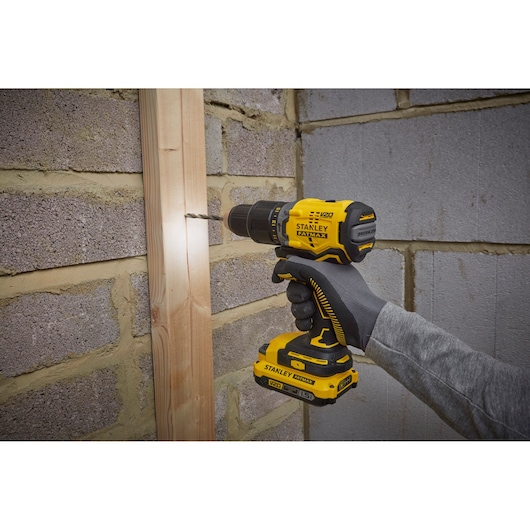 STANLEY SFMCD715C2K cordless drill in use on wood, yellow and black design, handheld power tool.