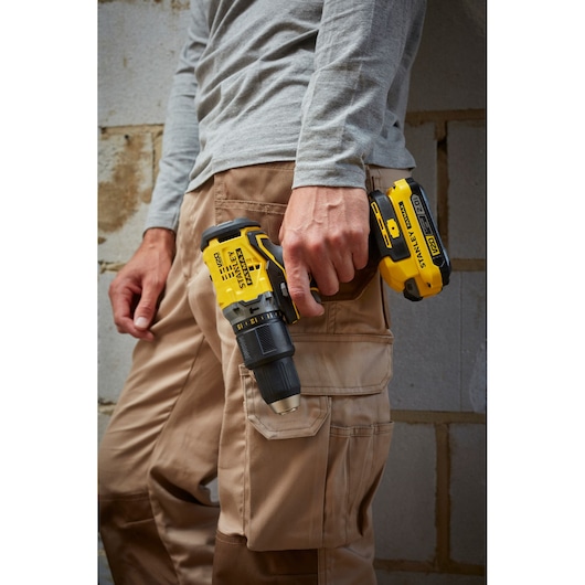 STANLEY SFMCD715D2F cordless drill held by worker in beige pants, close-up outdoor.