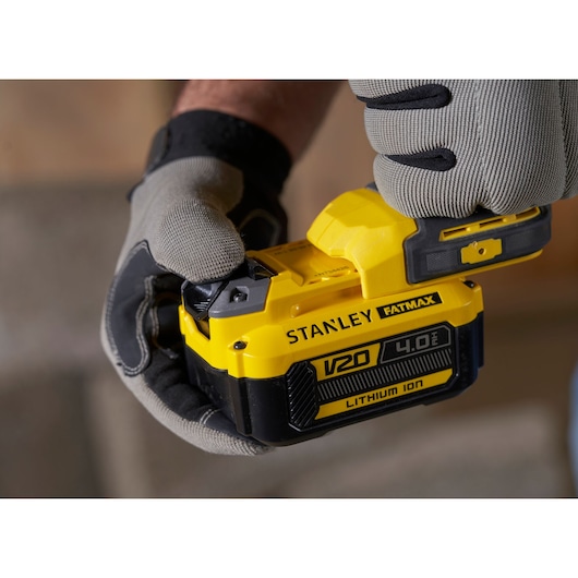 Photo of STANLEY SFMCD715M2K V20 FATMAX 4.0Ah lithium-ion battery held in gloved hands, close-up.
