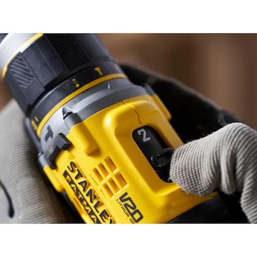 Photo of STANLEY SFMCD721B cordless drill speed setting, yellow and black tool held by gloved hand.
