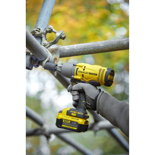 Photo of STANLEY SFMCF900B impact wrench used on scaffolding, yellow and black, V20 4.0Ah lithium-ion battery.