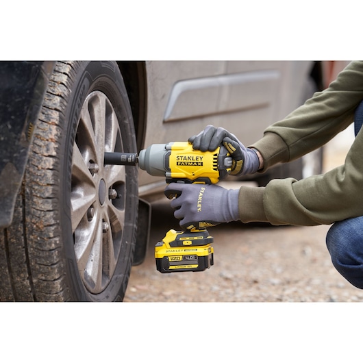 Photo of STANLEY SFMCF940M1 cordless impact wrench being used to tighten car wheel lug nuts outdoors.