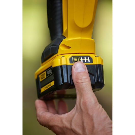 Close-up photo of hand pressing button on STANLEY SFMCHT855M1 cordless tool battery showing power indicator.