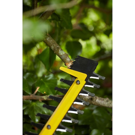 STANLEY SFMCHTB866B hedge trimmer blade cutting a tree branch, close-up, garden background.