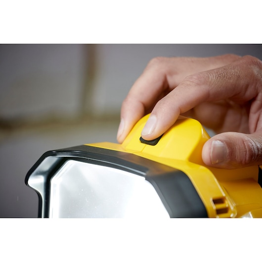 STANLEY SFMCL030B LED work light close-up, finger pressing power button, yellow and black housing.
