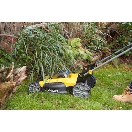 STANLEY SFMCMWS251B yellow cordless lawn mower in use cutting grass near plants outdoors.