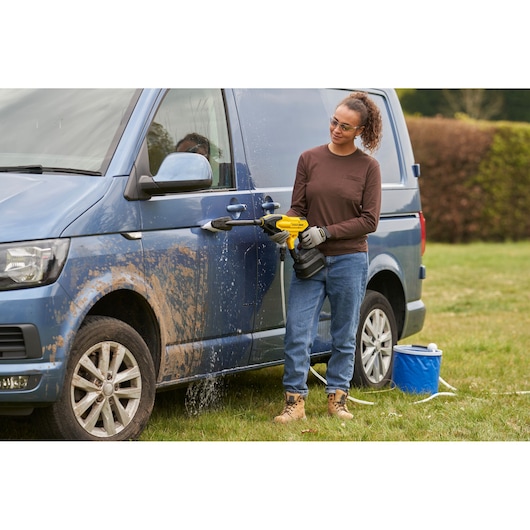 STANLEY SFMCPC93B portable washer used to clean muddy blue van outdoors, person holding tool.