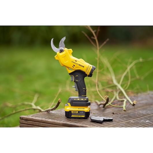 Photo of STANLEY SFMCPP32M1 cordless pruning shears with V20 lithium battery on a wooden surface outdoors.