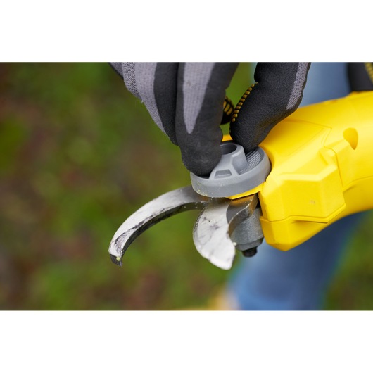 STANLEY SFMCPP32M1 yellow pruner close-up with gloved hand adjusting gray dial outdoors.