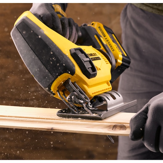Photo of STANLEY SFMCS600M2K cordless jigsaw in use, cutting wood, close-up of tool and gloved hands.