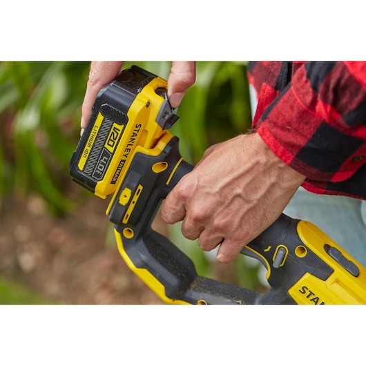 STANLEY SFMCST933B cordless tool close-up, person inserting V20 4.0Ah lithium-ion battery outdoors.