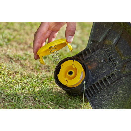 STANLEY SFMCST933B string trimmer spool cover and spring shown on grass, close-up angle.