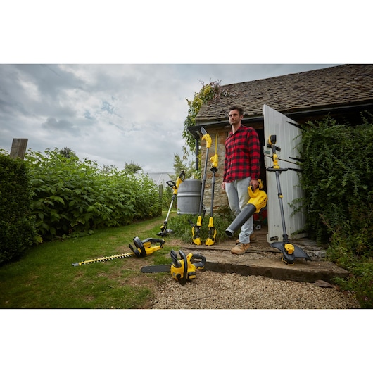 STANLEY SFMCST933B garden power tools in use outdoors near cottage, including trimmer, blower, hedge trimmer.