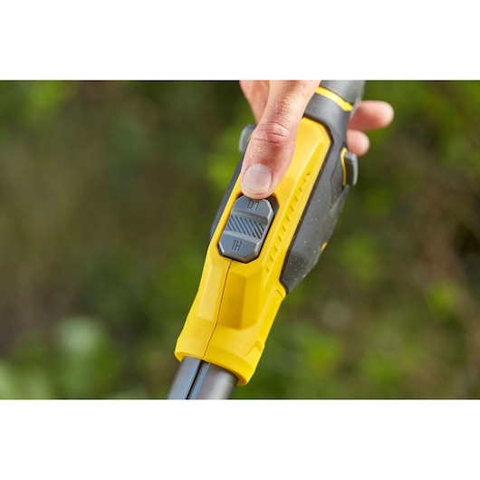 STANLEY SFMCSTB933B trimmer close-up of yellow and black handle with speed switch and thumb operation outdoors.