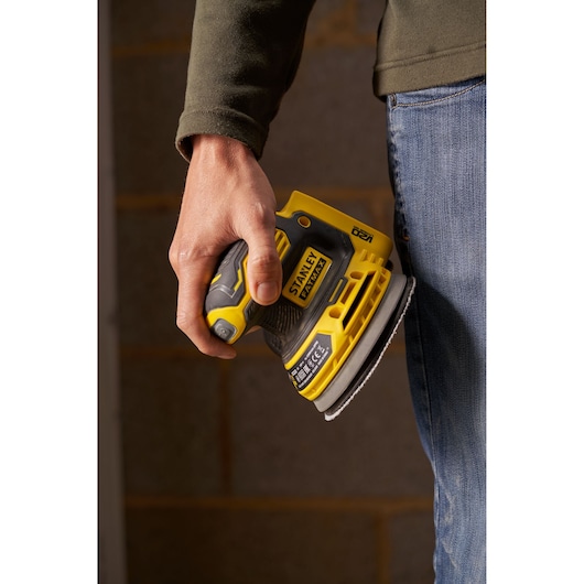 Photo of STANLEY SFMCW220D1S cordless sander in hand, yellow and black, close-up view.