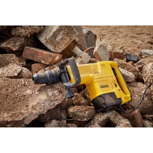STANLEY SFMEH230K-QS demolition hammer resting on rubble, yellow body with black handle, side view.