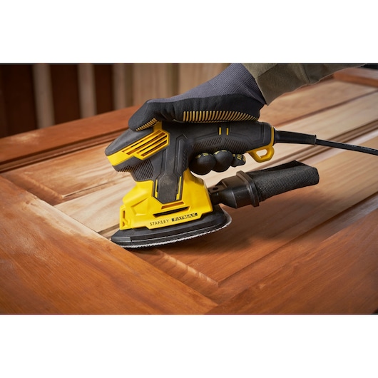 Stanley SFMEW210S sander used on wood surface, close-up, yellow and black design, power tool photography.