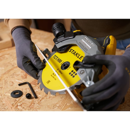Stanley STA13030 circular saw blade installation on wood surface, close-up with gloved hands and tool parts.