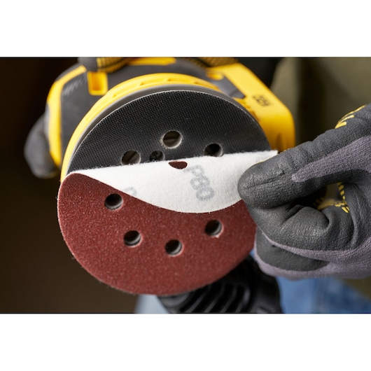 STANLEY STA32392 sanding disc being attached to a yellow power sander, close-up angle, product photography.