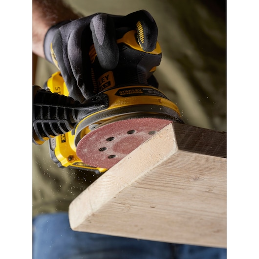 STANLEY STA32392 sander in use on wood, close-up showing gloved hand and sanding disc.