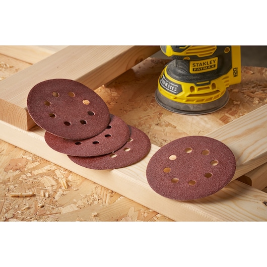 STANLEY STA32392 sanding discs and sander on wooden boards, front angle, brown discs with holes.