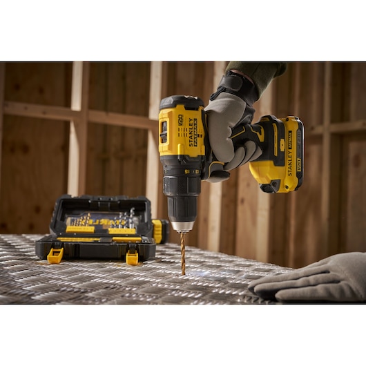 Stanley STA88550 cordless drill in use, yellow and black, with drill bit kit, workshop background.
