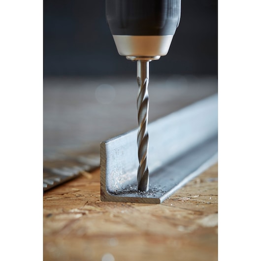 STANLEY STA88553 drill bit making a hole in a metal angle bar, close-up photo on wooden surface.