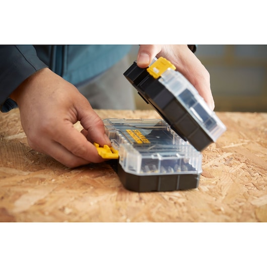 STANLEY STA88555 storage box with clear lid and yellow latch held by hands, on wood surface.