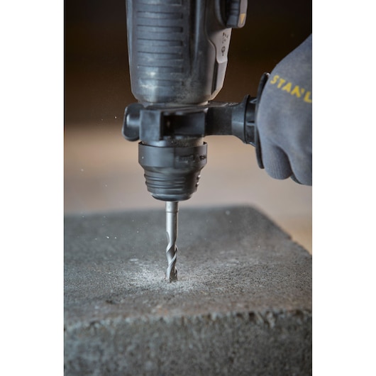 STANLEY STA88555 drill bit in rotary hammer drilling into concrete block, close-up side view.