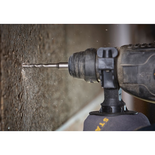 STANLEY STA88555 drill in action drilling into concrete wall, side angle, visible dust particles, Photography.