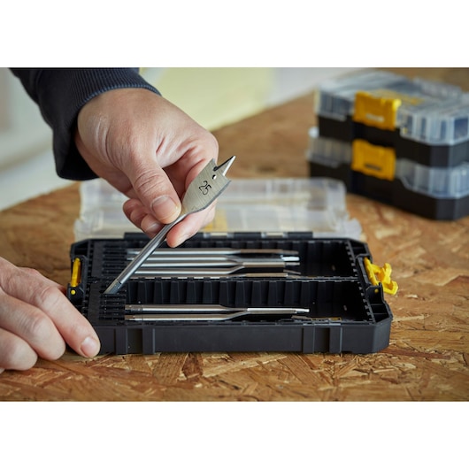 STANLEY STA88556 drill bit set in black case, hand holding flat wood drill bit, case open on wood surface.