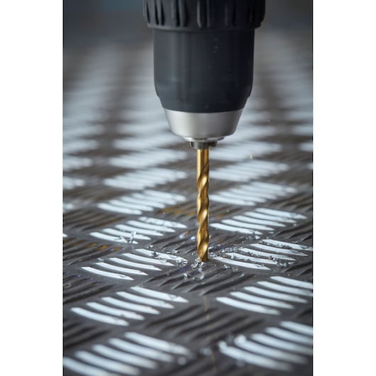 STANLEY STA88563 drill bit in a power drill drilling into a textured metal surface, close-up photography.