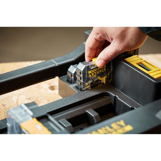 Photo of a hand placing a STANLEY STA88567 digital device into a black and yellow tool storage tray.