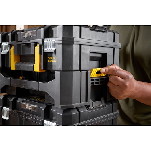 STANLEY STA88580 black and yellow PROSTACK toolbox, close-up side angle, hand pressing yellow latch.