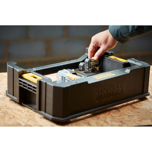 Photo of STANLEY STA88580 tool battery storage box with a hand inserting a battery, shown on a wooden surface.