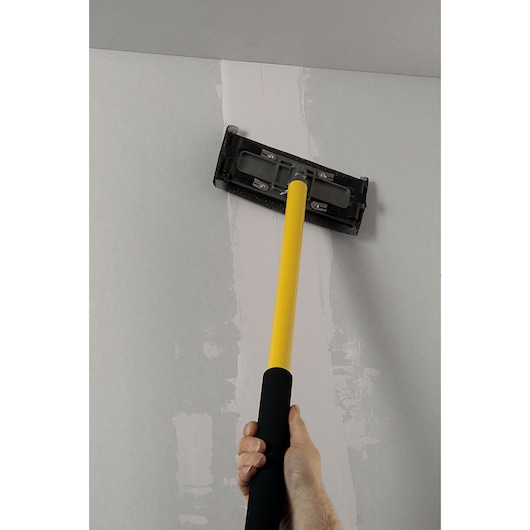 STANLEY STHT0-05928 drywall sander with yellow handle used on ceiling, close-up photography.