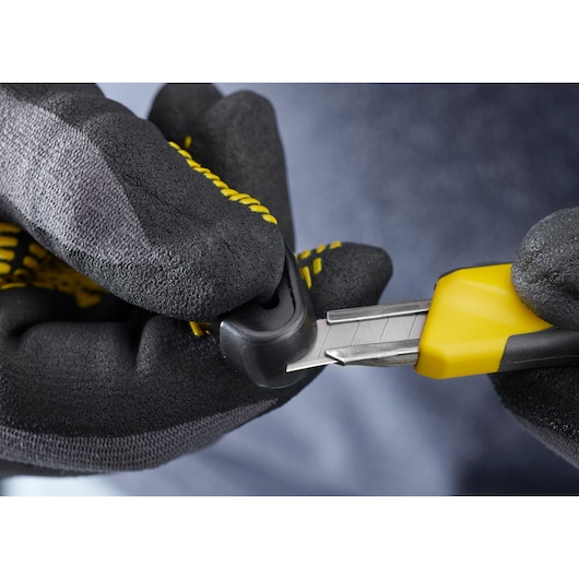 Photo of STANLEY STHT0-10264 utility knife with yellow and black handle, being held with gloved hands, close-up.